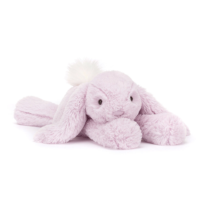 A plush lavender-colored Jellycat Bashful Beige Bunny with a fluffy cream bobtail, lying down.