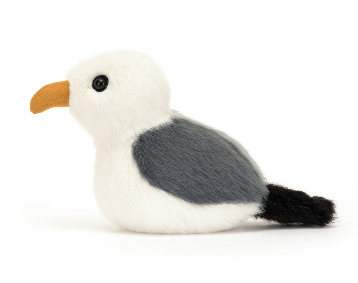 A seagull plush toy with soft fur in cream, grey, and black, and a suedette mustard beak.