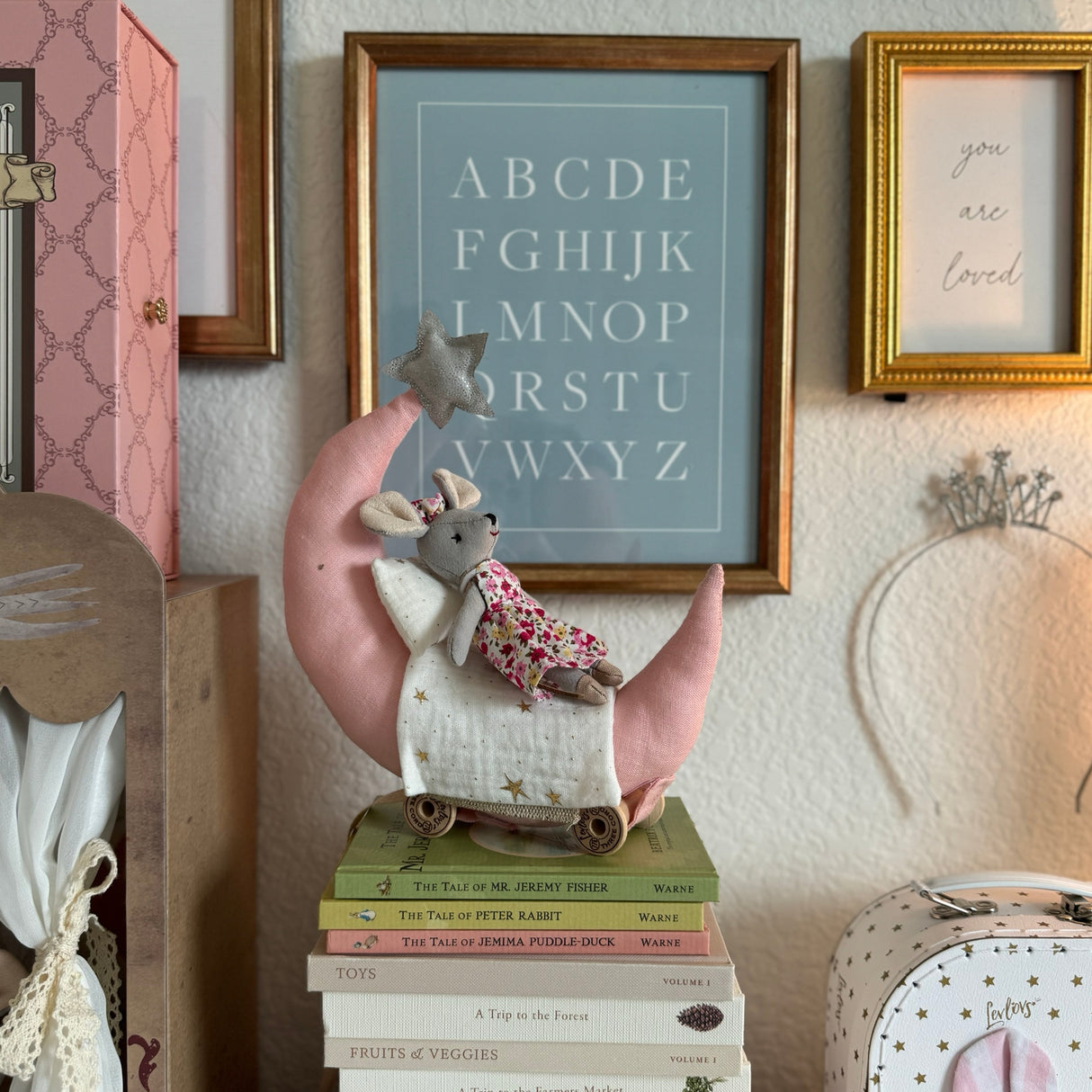 Decorative wall with framed alphabet poster, toy mouse, and books.