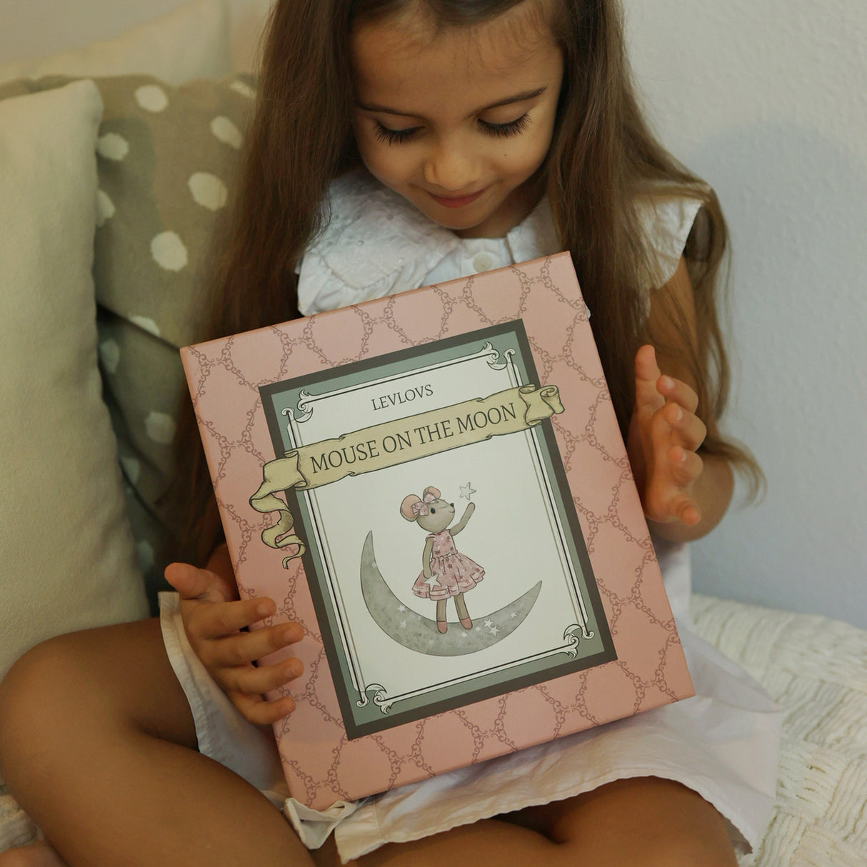 Child holding a box titled 'Mouse on the Moon' with a pink cover.