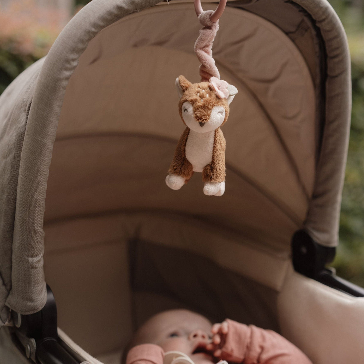 Baby in a pram with a plush deer toy hanging above