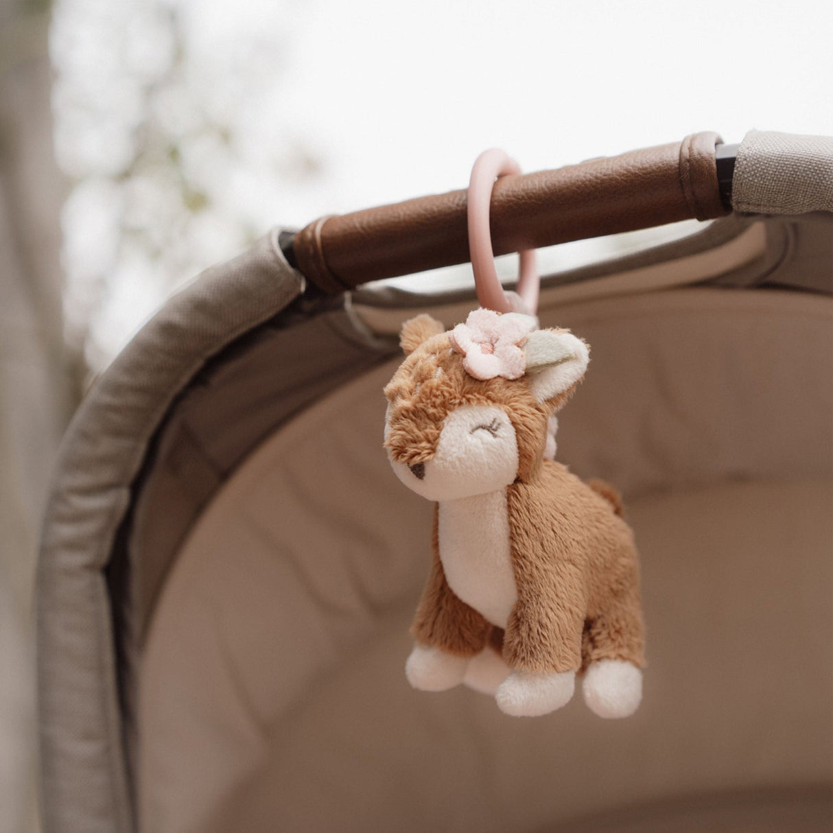 Plush shake deer toy hanging from a pram handle with a blurred background