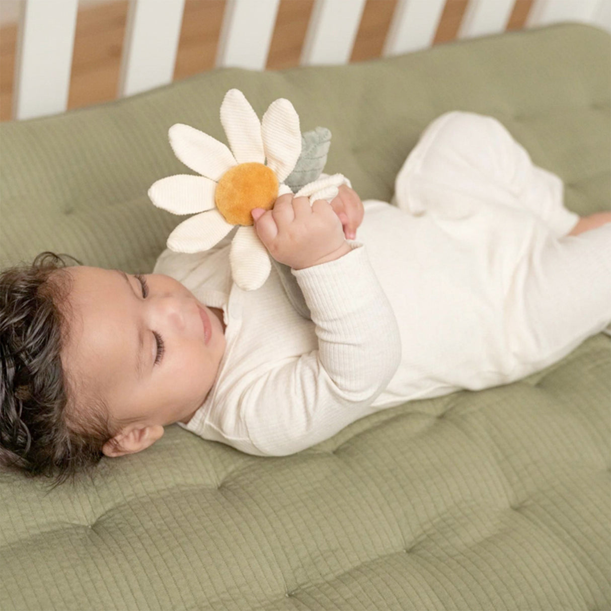Baby lying on a green cushion holding a white flower toy.