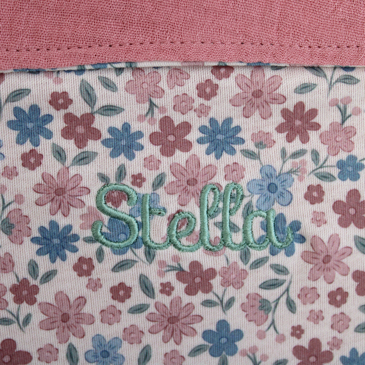 Floral patterned fabric with name embroidered in green thread on a pink background