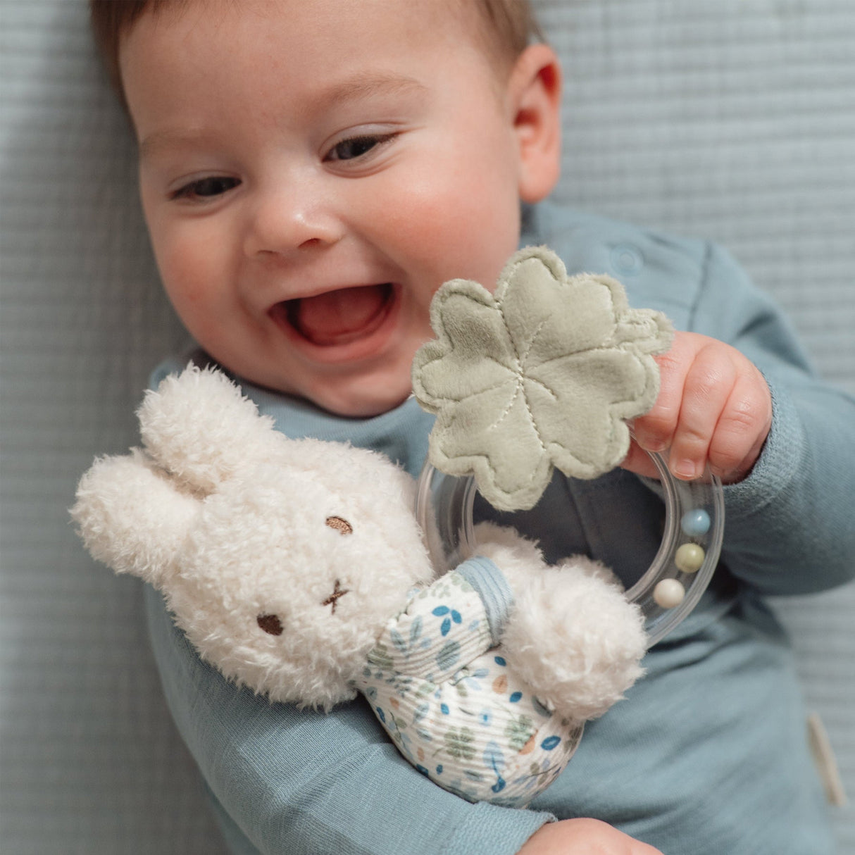 Baby laughing holding a soft Miffy toy rattle with Little Dutch Lucky print clothing and a ring rattle with tiny beads and a soft leaf