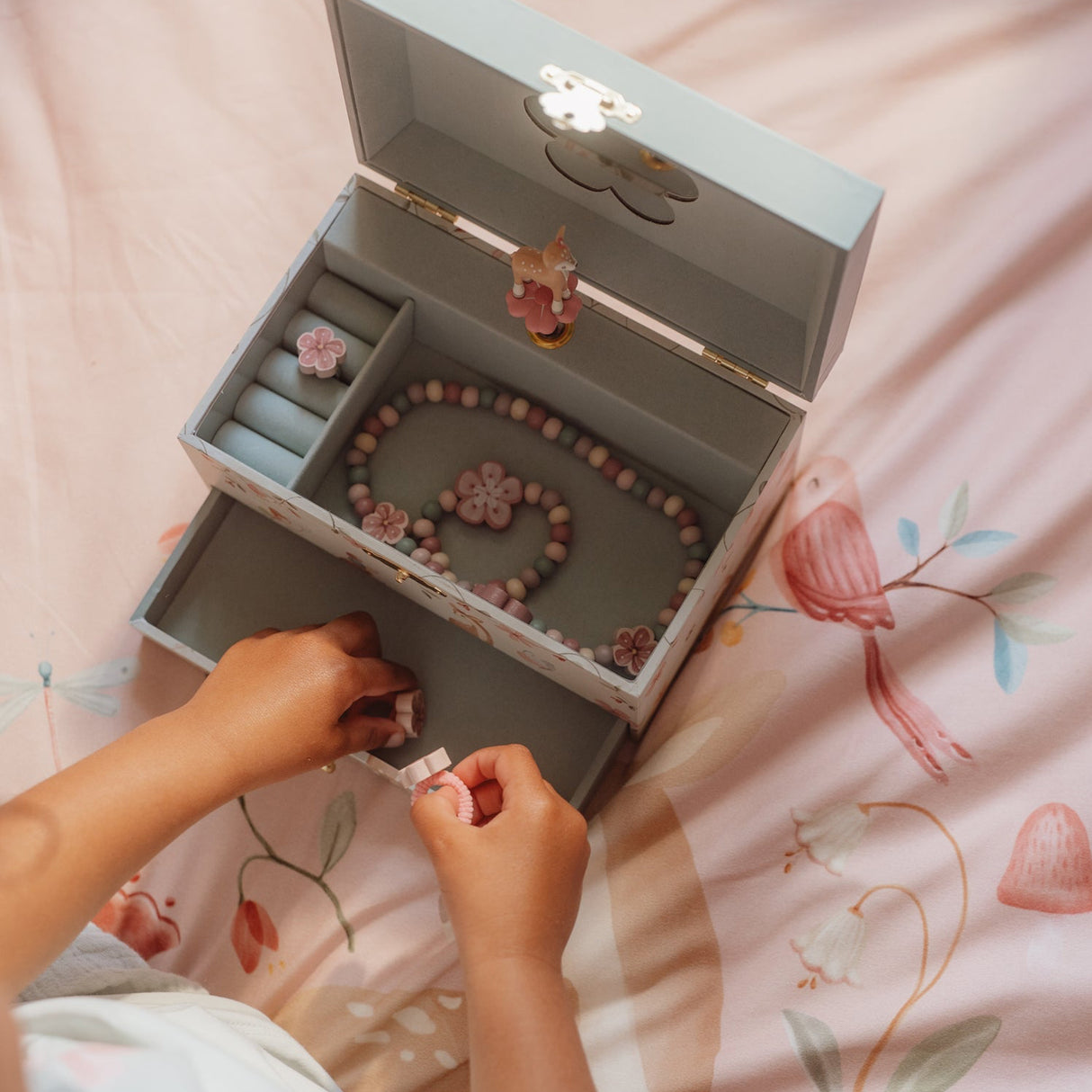 Child organizing jewelry in a decorative box on a floral bedspread
