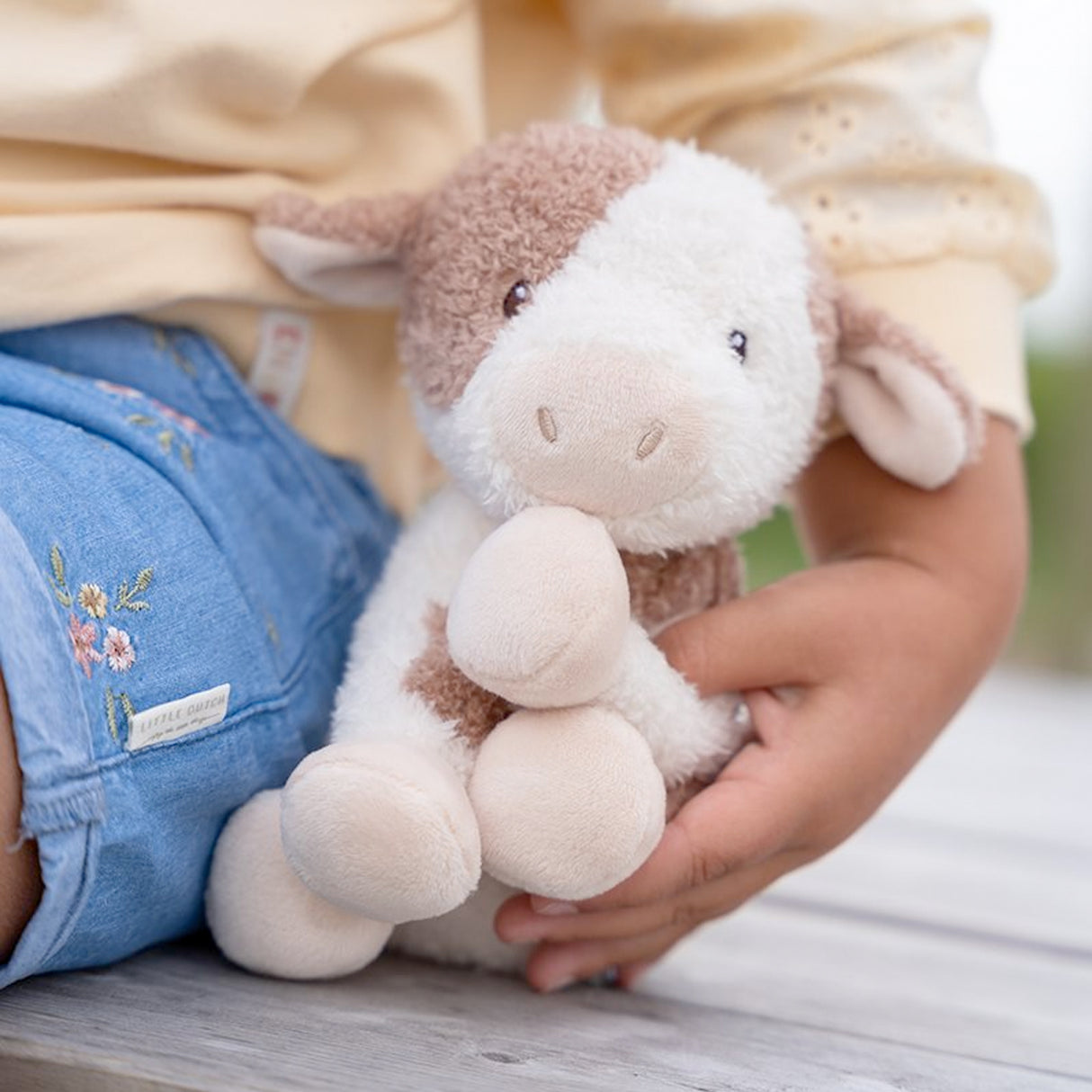 Child holding a Little Duth plush toy in their lap with a blurred background