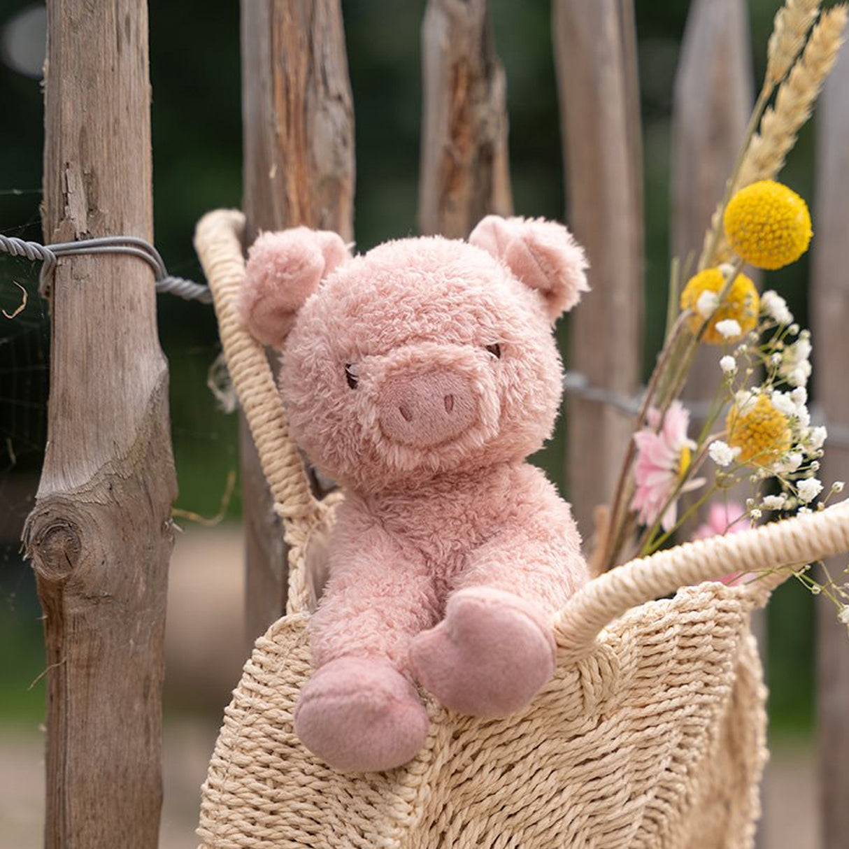 Pink pig plush toy in a basket with flowers