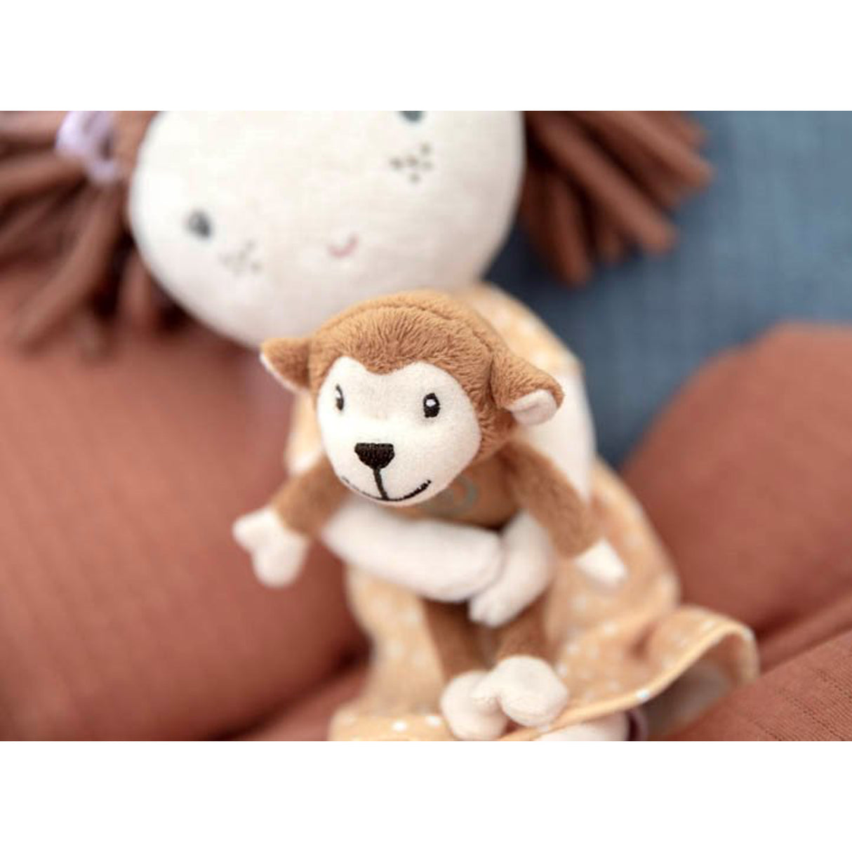 Small plush monkey toy with a soft doll toy in the background