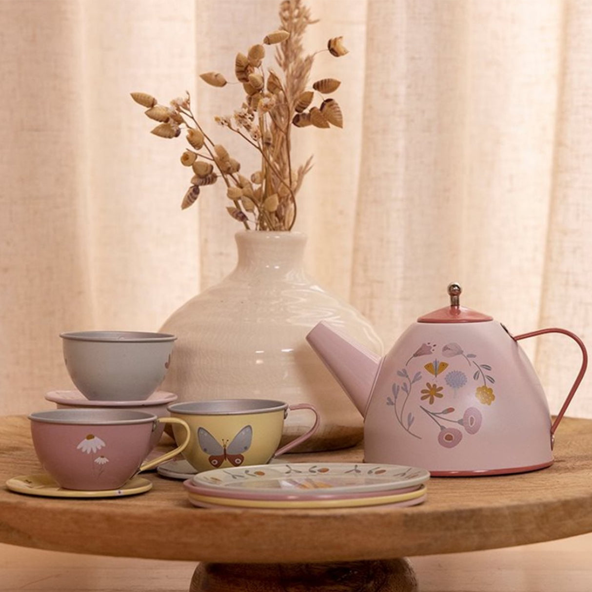 Metal teapot and cups with floral design on a wooden table against a beige curtain background