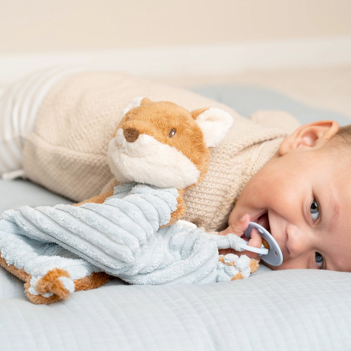 Child holding a Little Dutch Plush fox cuddle cloth toy with a dummy clip in a crib
