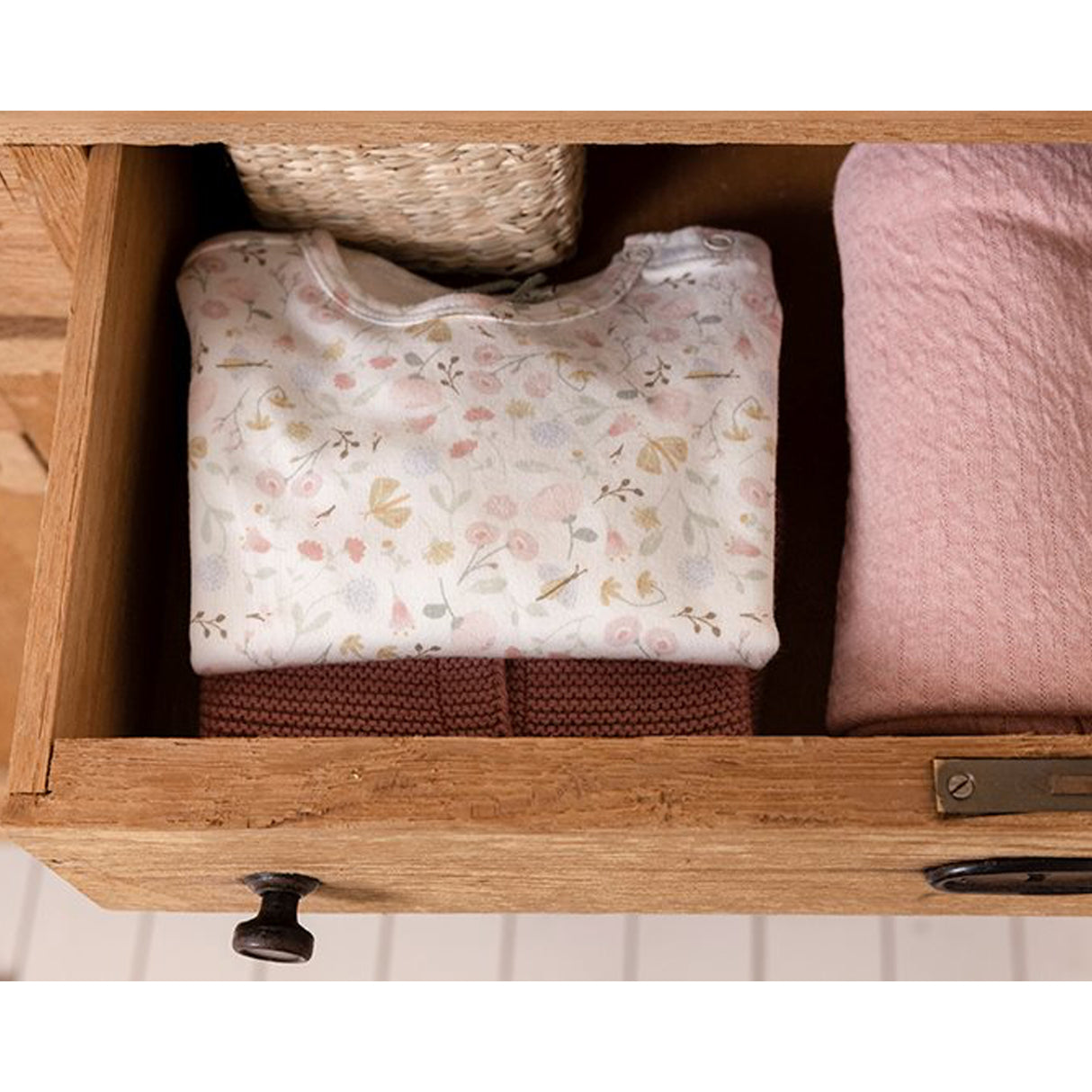 Little Dutch floral baby bodysuit folded in an open wooden drawer with soft pink blanket