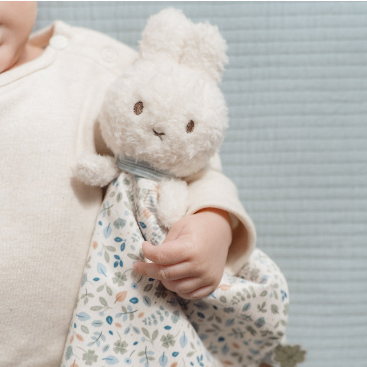 Child holding a soft toy with a floral blanket against a neutral background