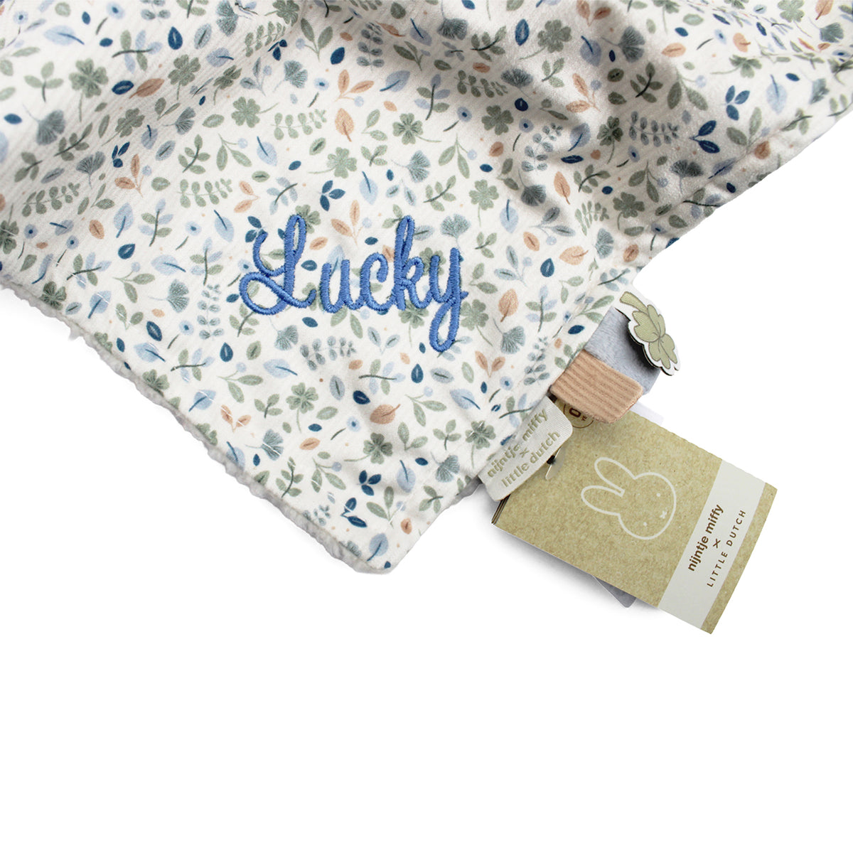 Close-up of a baby comfort blanket with a white background and a delicate blue, green, and beige floral pattern. A name is embroidered in blue script on the pattern.