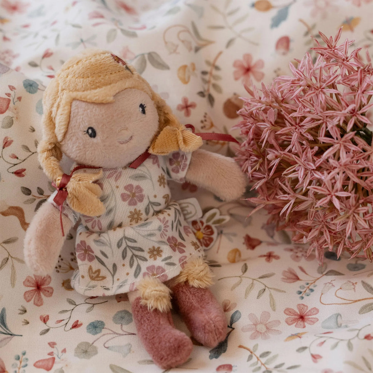 Soft mini doll with floral dress and yellow hat on a floral fabric background