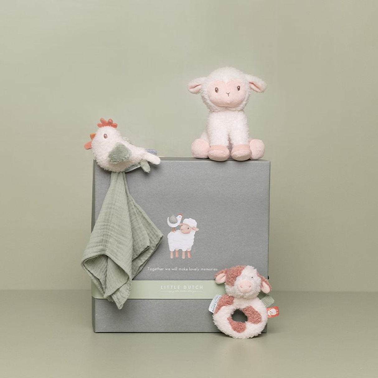 Set of baby toys including a plush lamb, chicken soother, and cow ring rattle, with a dark sage green box on a light green background.