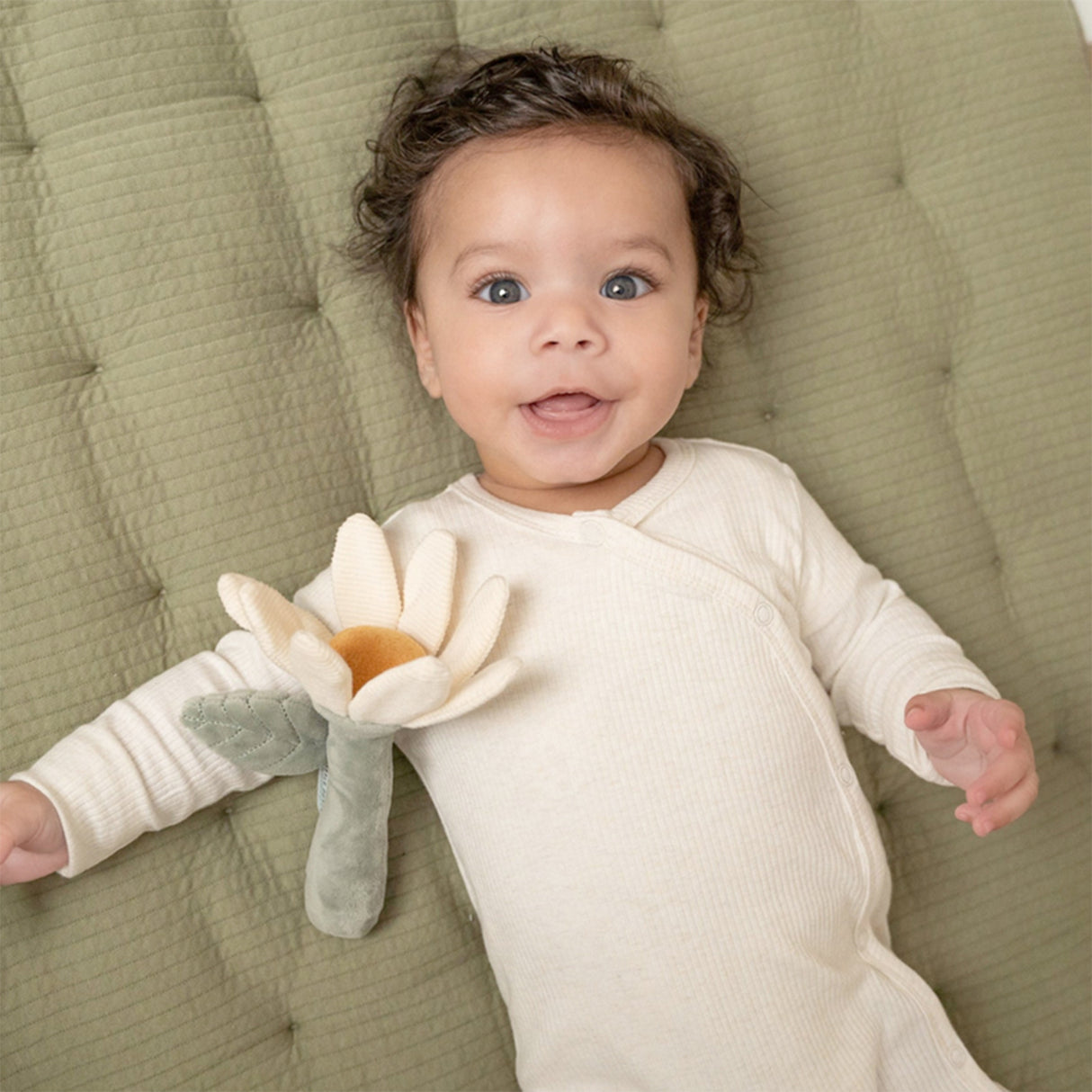 Baby lying on a green cushion holding a flower shaped soft toy