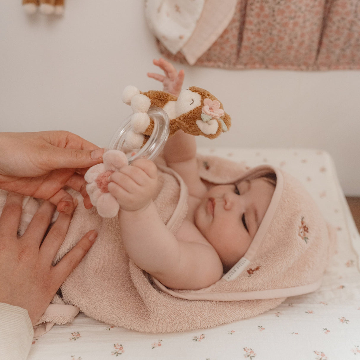 Baby wrapped in a towel with a rattle, lying on a floral blanket