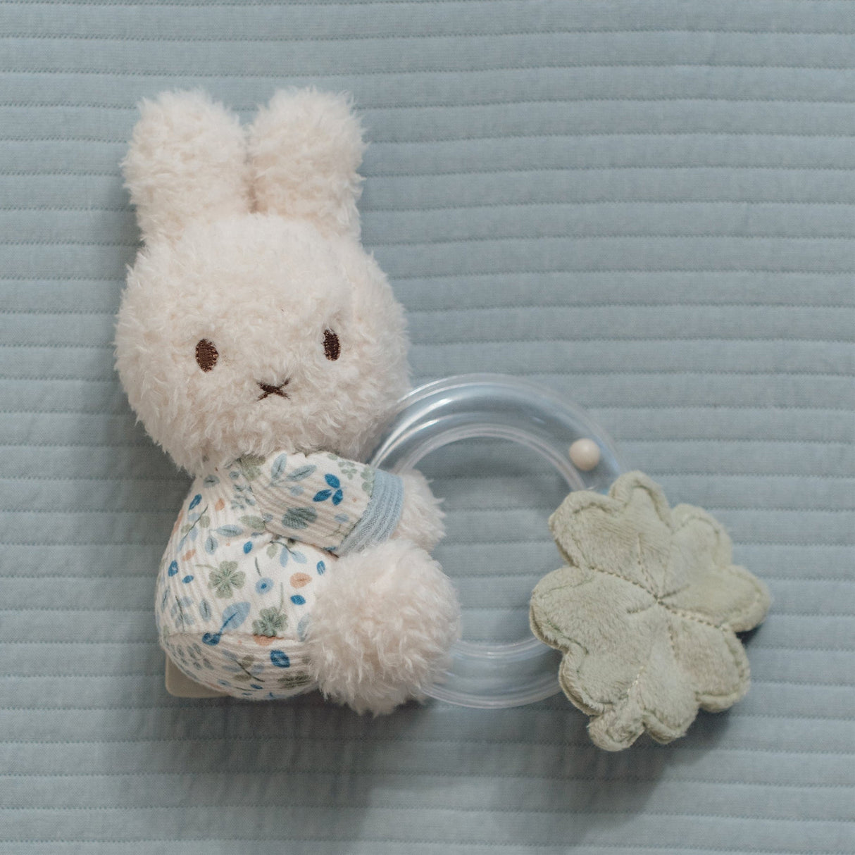 White plush miffy bunny with a floral outfit and clear rattle on a textured blue surface