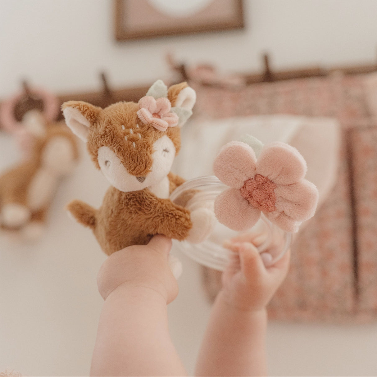 Child's hand holding a plush deer toy with a flower in a nursery setting
