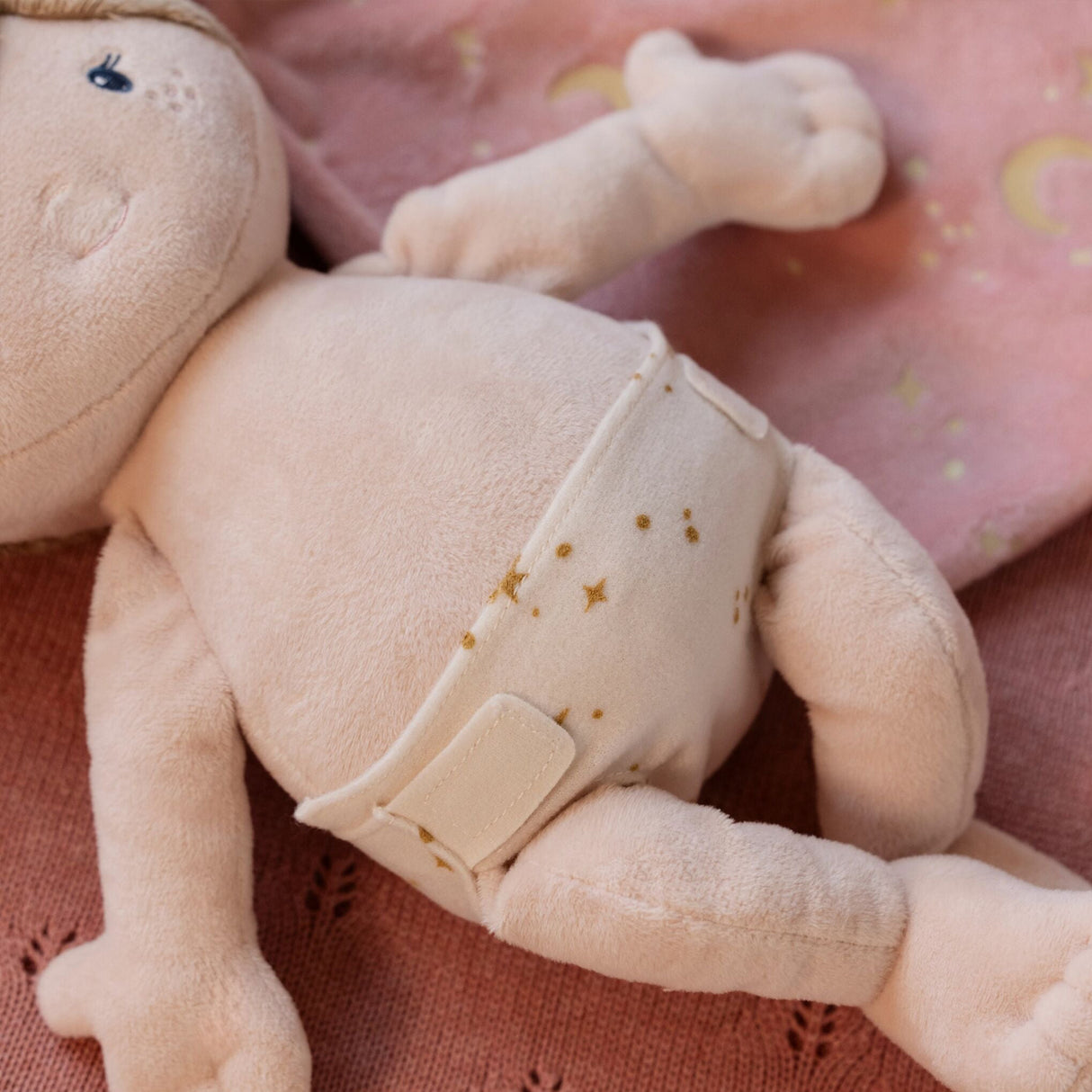 Soft baby doll with a nappy on a pink textured background