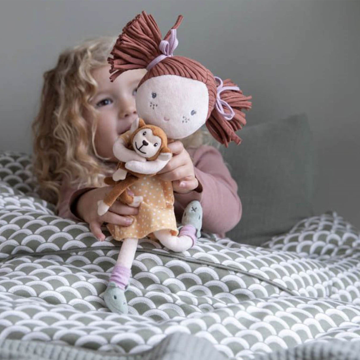 Child holding a rag doll hugging a monkey on a bed