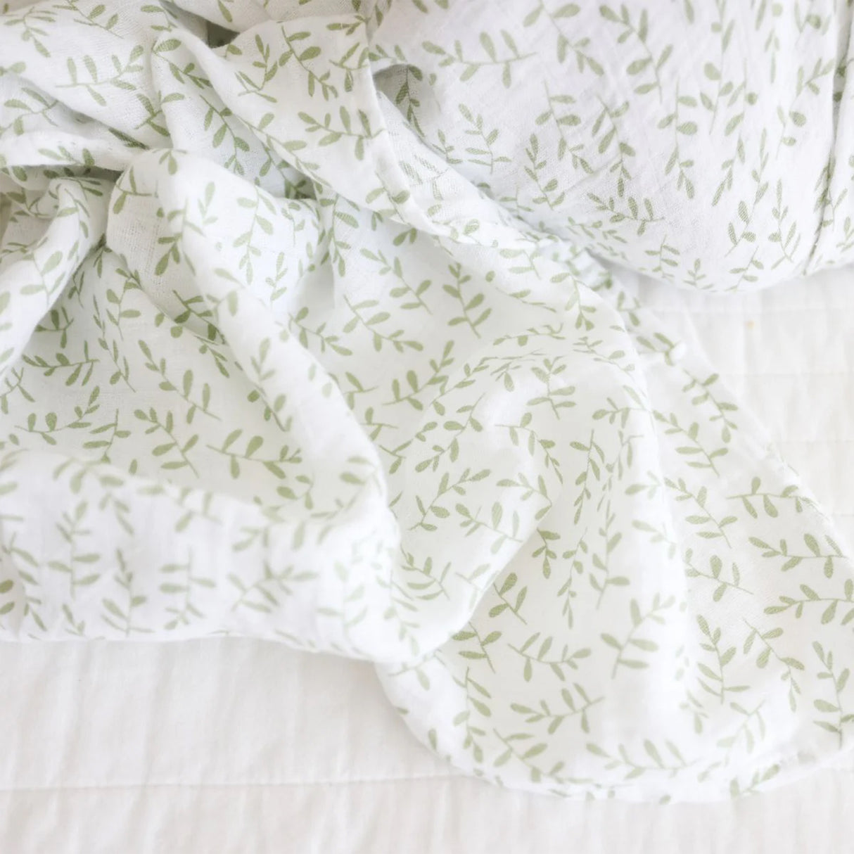 White cotton muslin baby swaddle with green leaf pattern on a white background