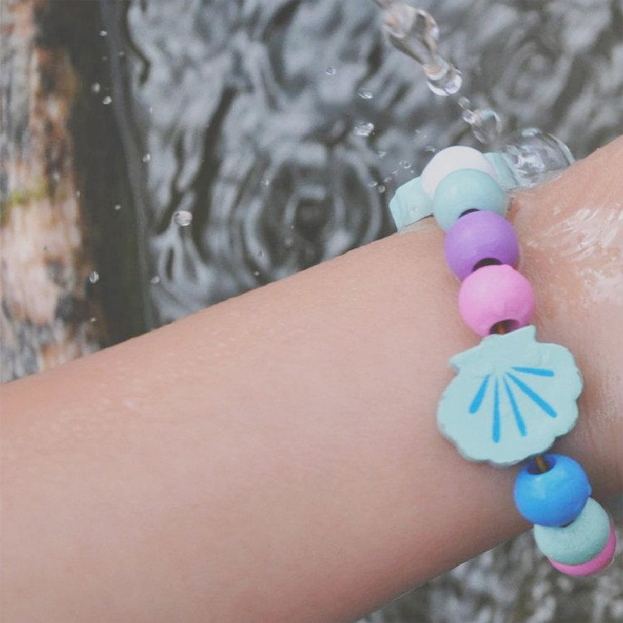 cotton twist Colorful beaded bracelet with a shell charm on a wrist, against a water background