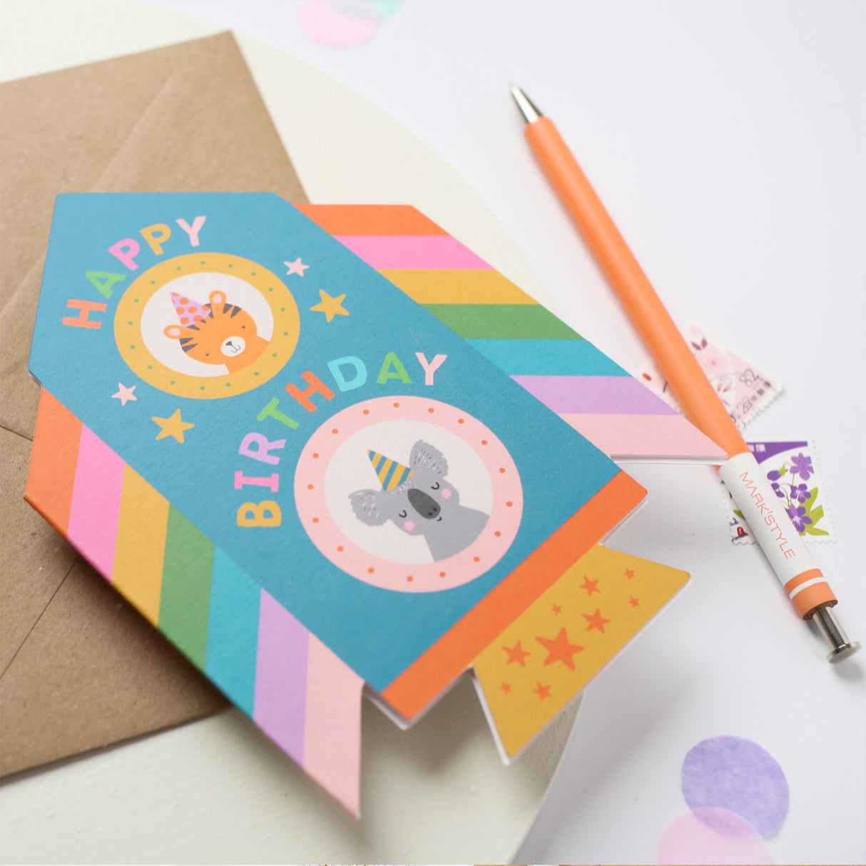 Colorful birthday card with cartoon animals, envelope, and pen on a light background