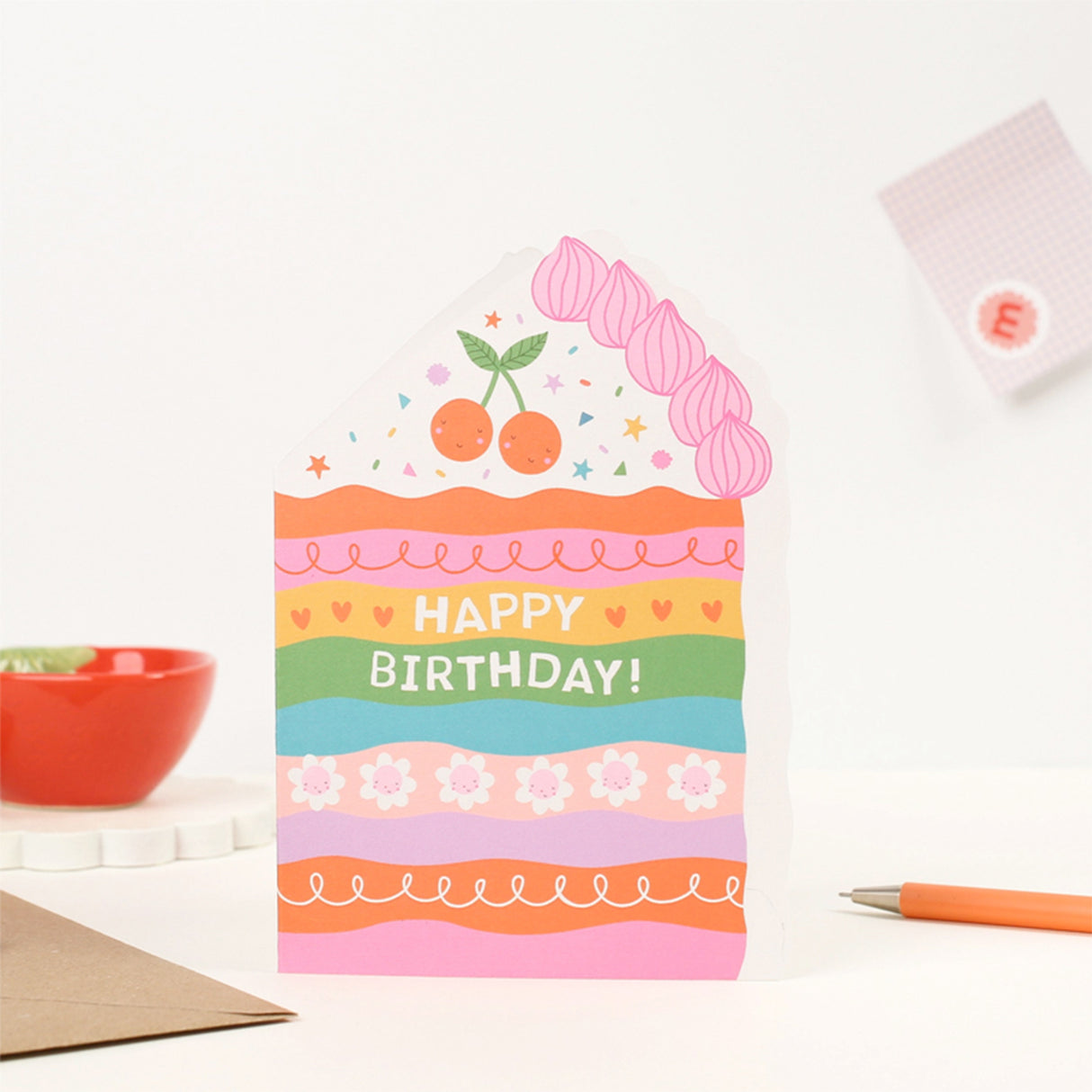 Mifkins Colorful birthday card with cake design on a white surface with stationery items.