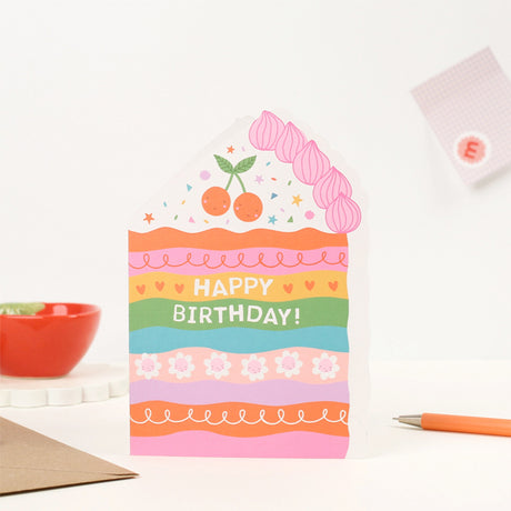 Mifkins Colorful birthday card with cake design on a white surface with stationery items.
