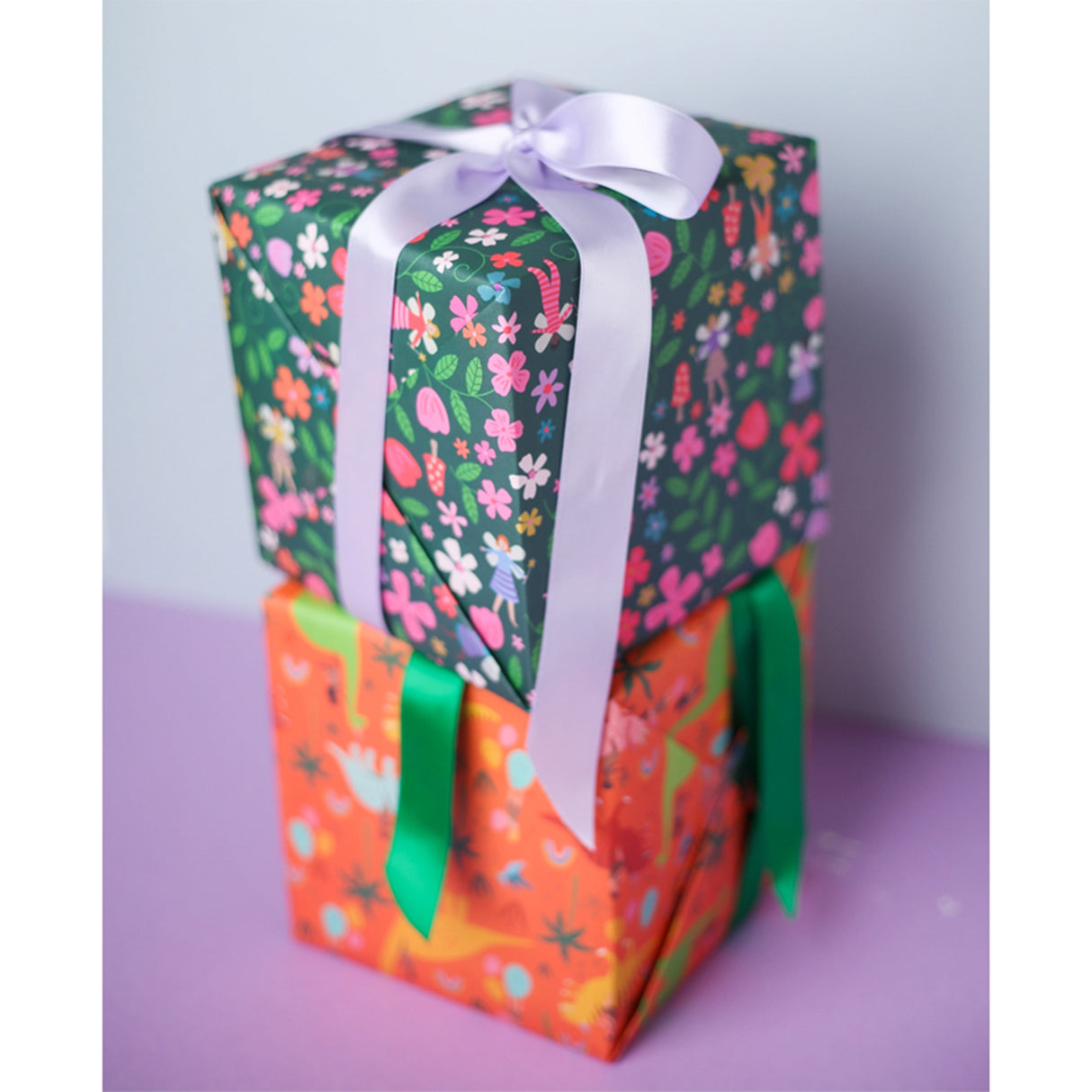 Two gift boxes with colorful patterns and ribbons on a light purple background