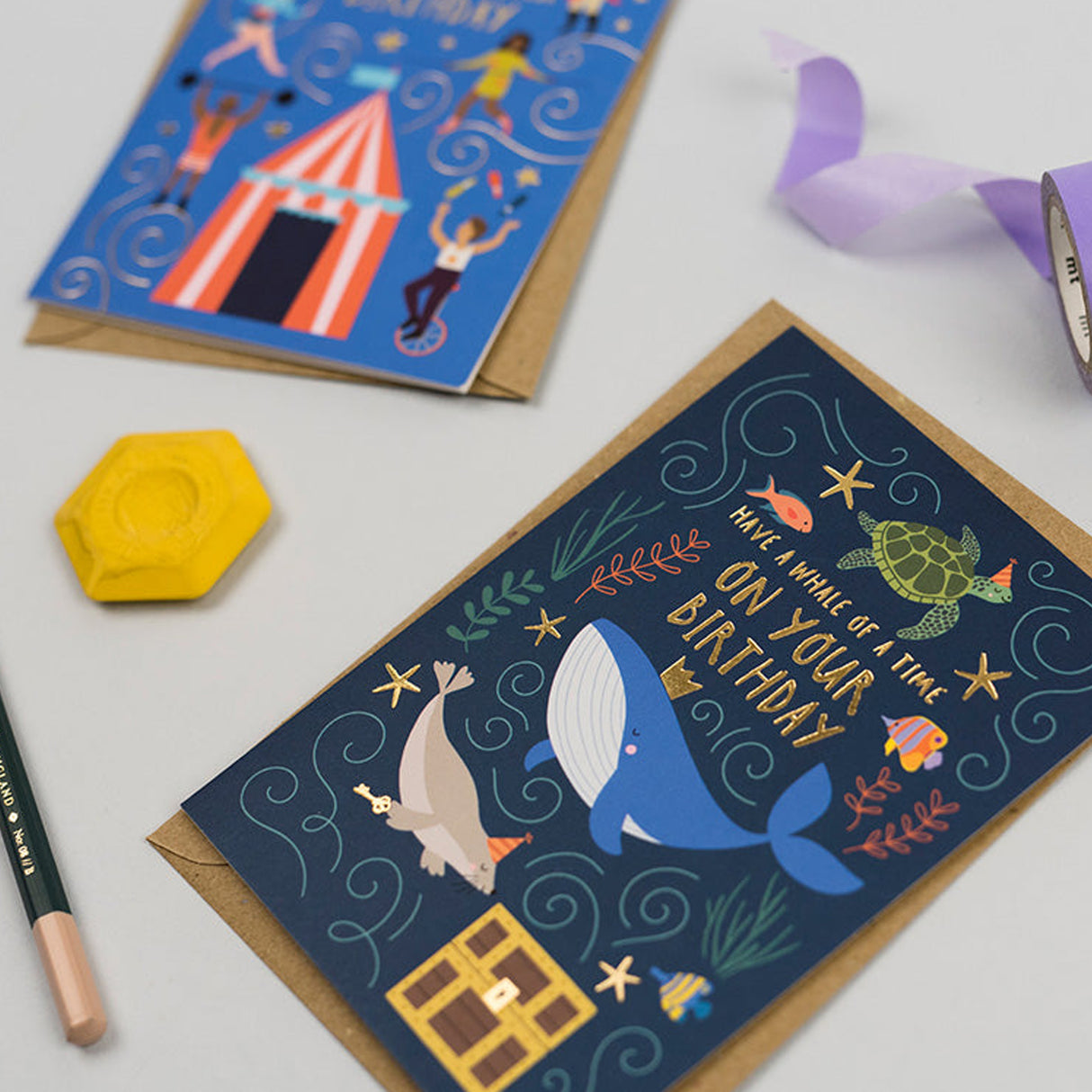 Birthday card with whale illustration on a white surface with stationery items.