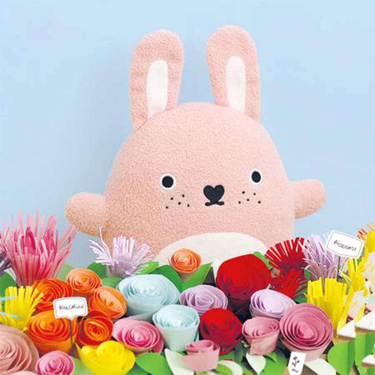 Soft pink toy rabbit surrounded by colourful flowers on a light blue background