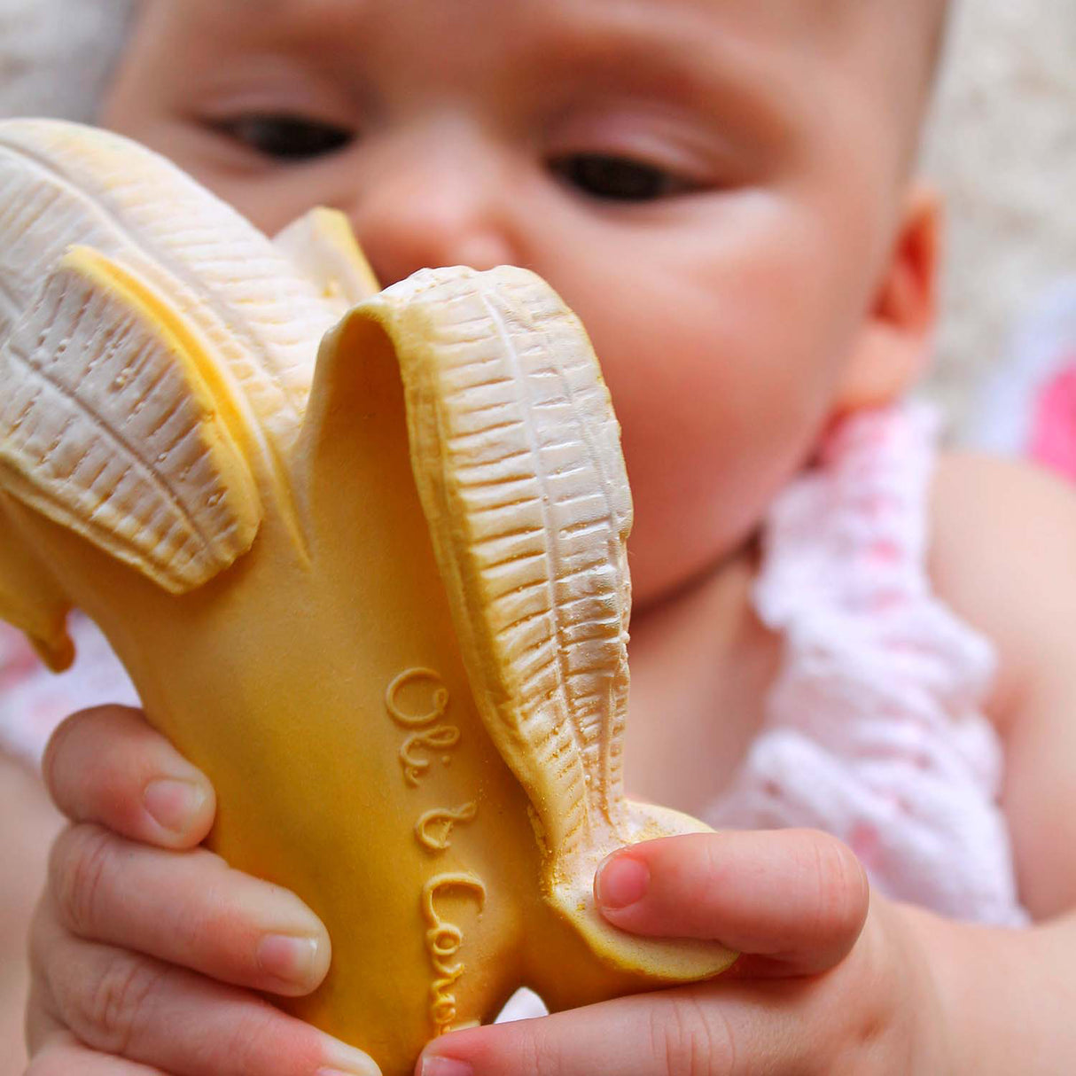 Baby holding a banana-shaped toy with 'Ol & Co' branding