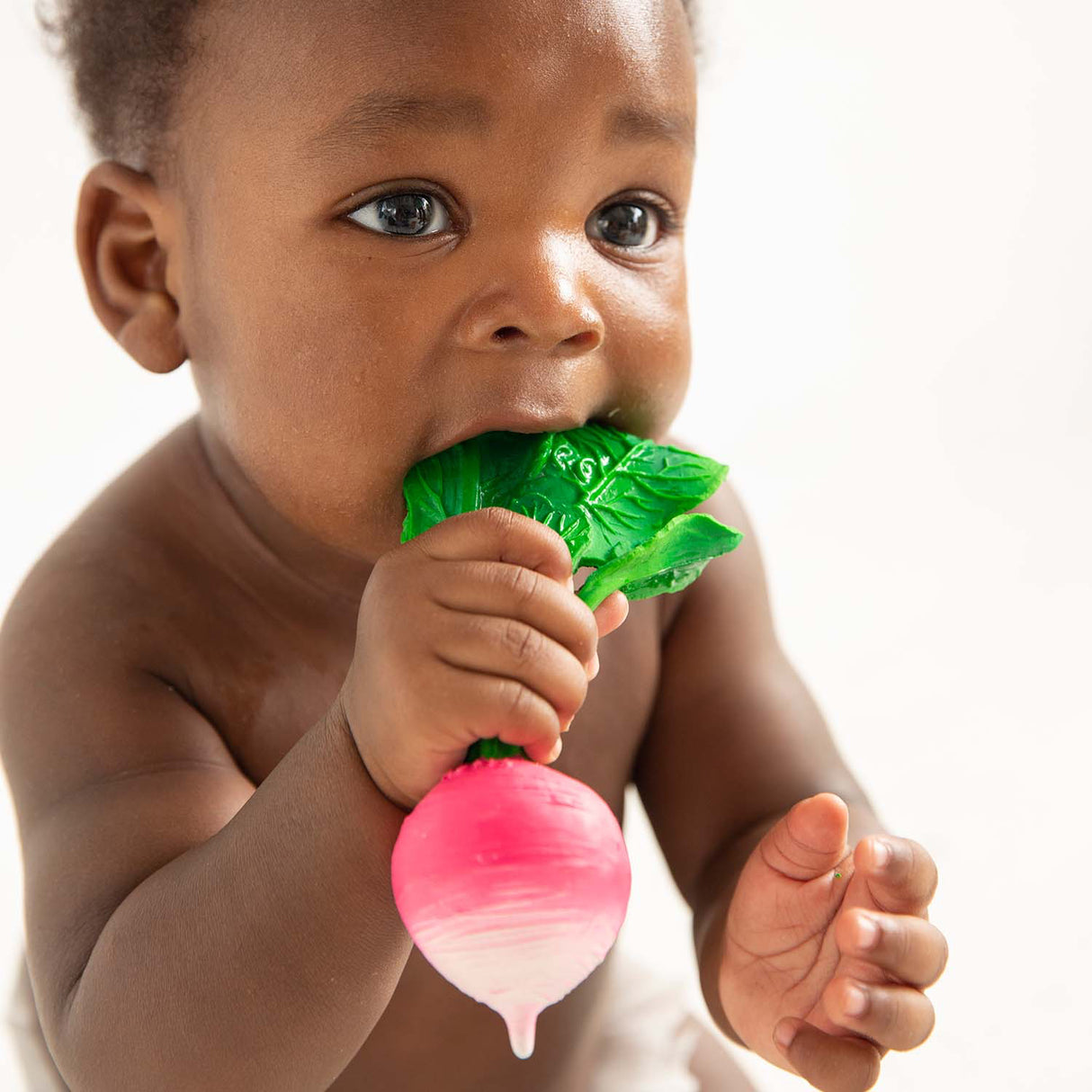 Baby chewing on teether rattle in the shape of a pink raddish