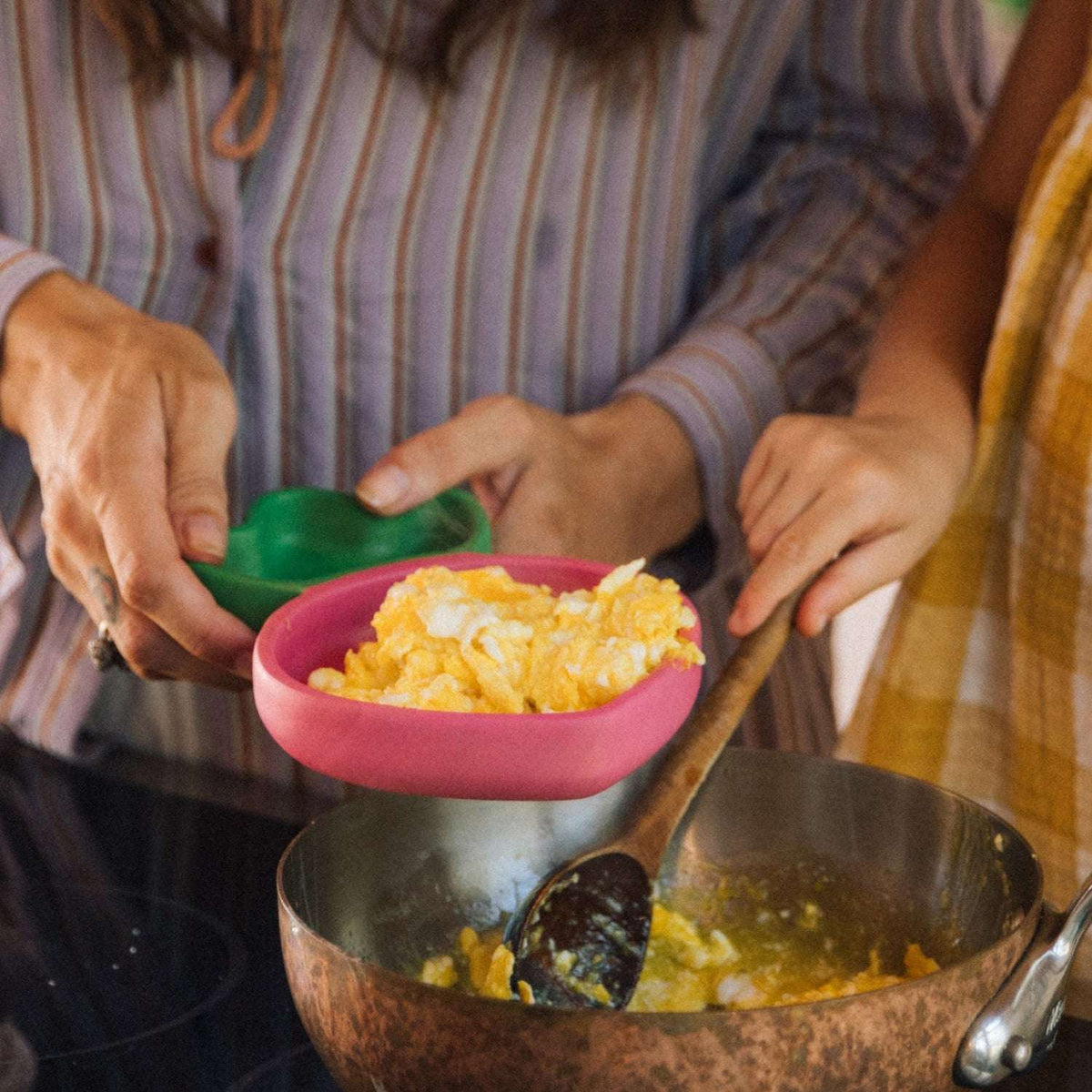 Person cooking scrambled eggs in a pan and eggs in the raddish shaped wooden bowl