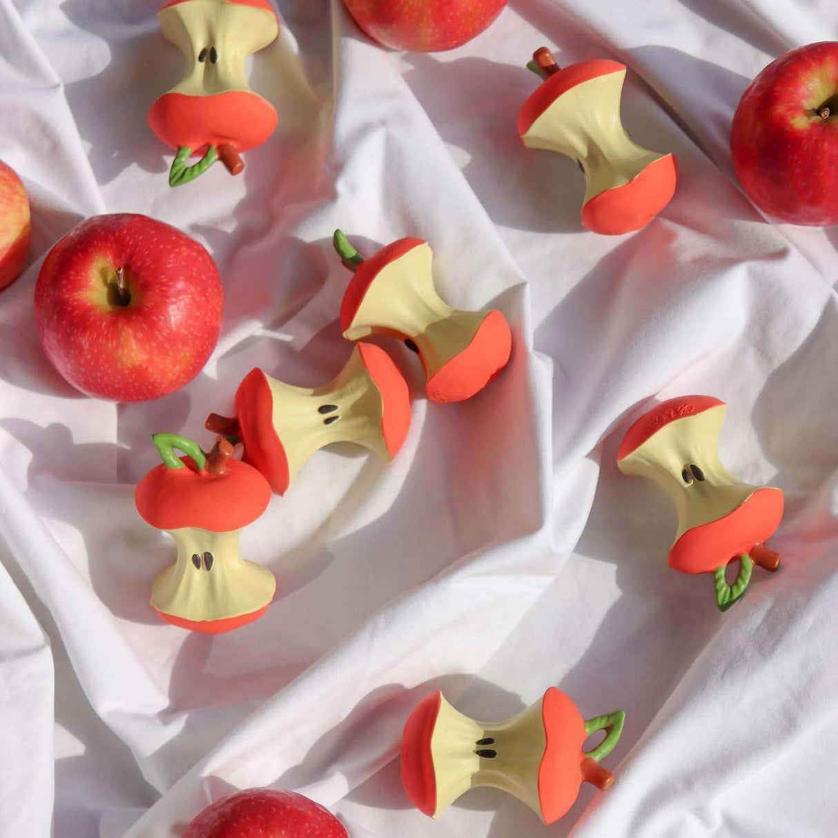 Red apples and apple-shaped teething toys on a white fabric background