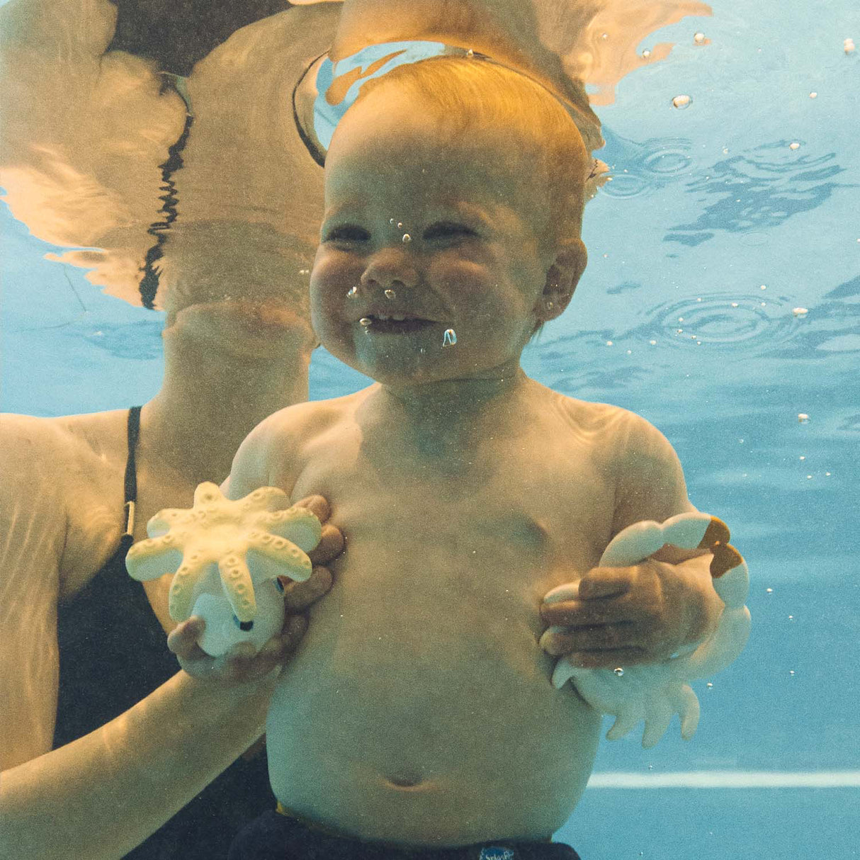 Child underwater holding octopus, smiling.