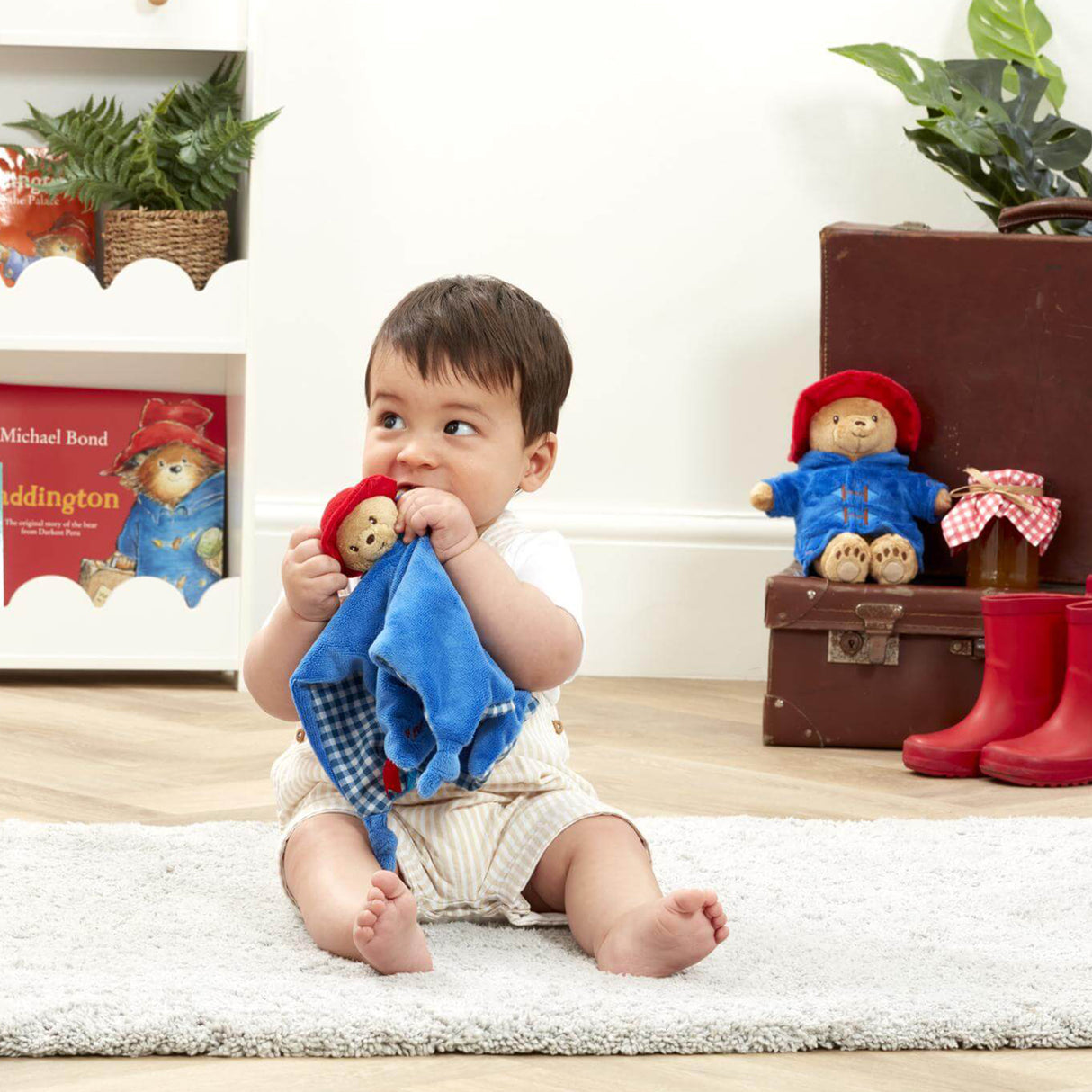 Child sitting on rug with a blue Paddington Bear baby comfort blanket