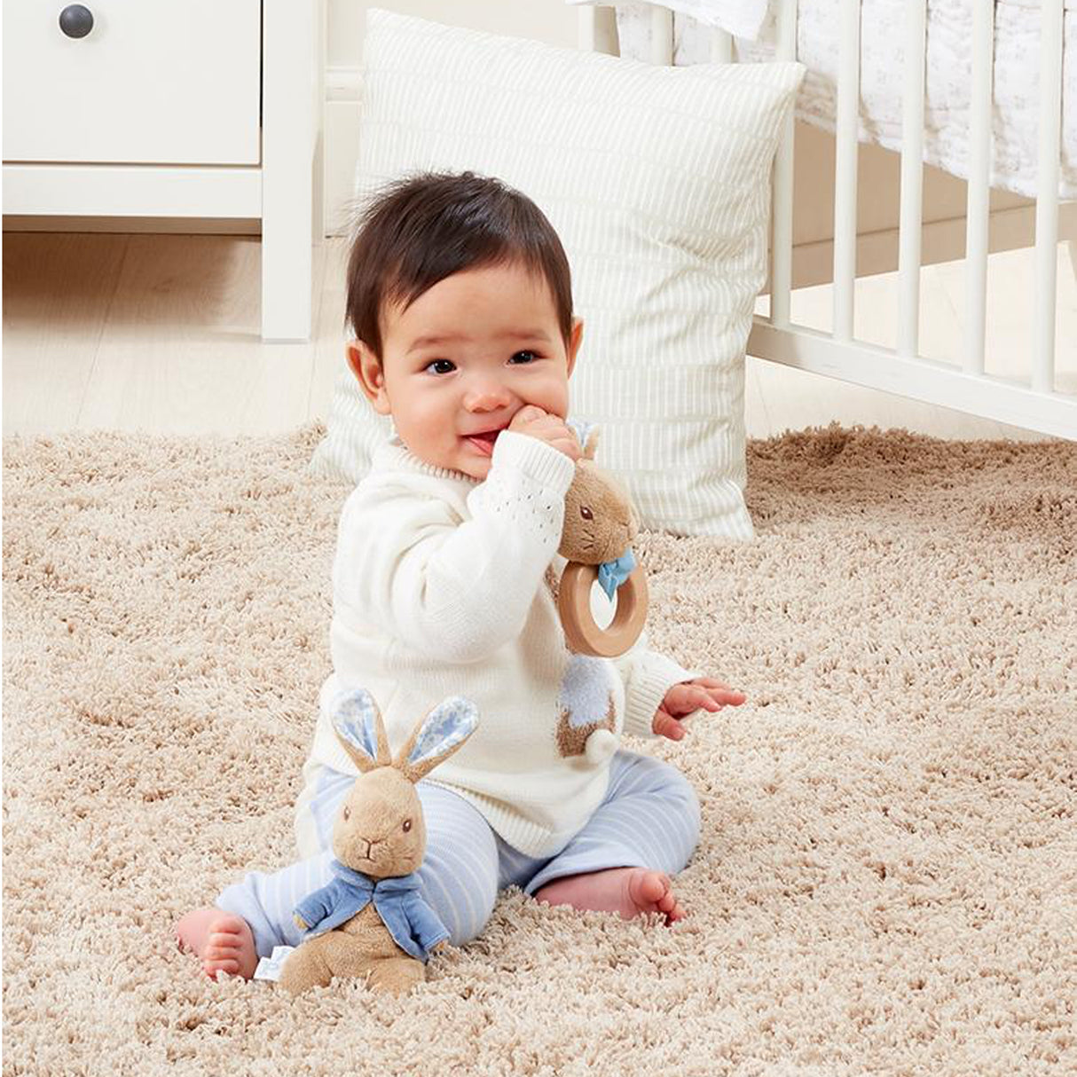 Baby sitting on a carpeted floor with plush toys in a nursery setting