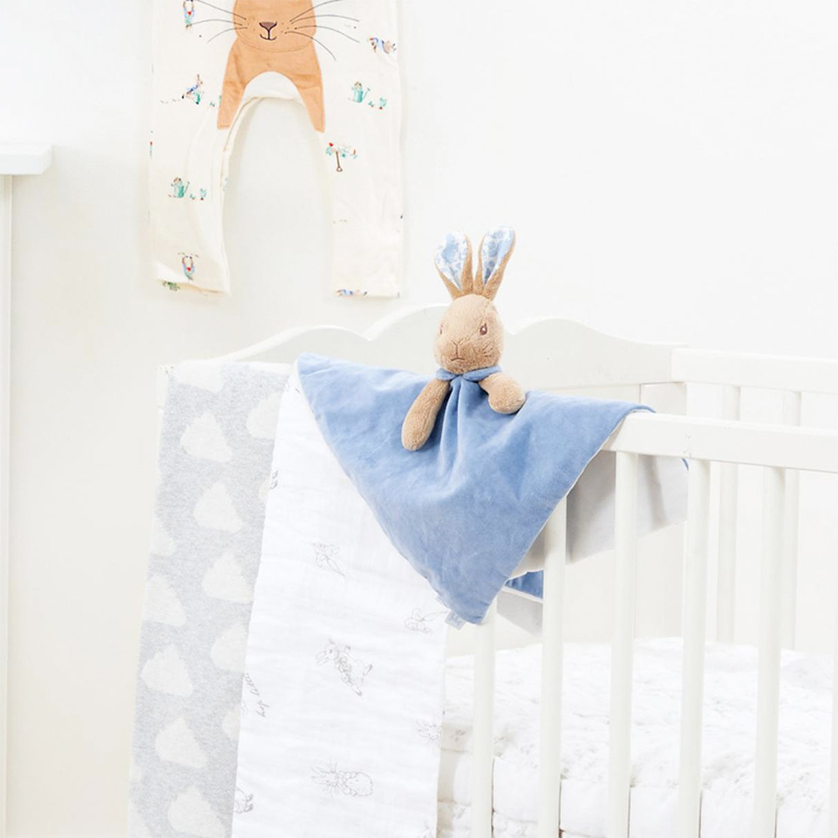 Baby crib with a blue Peter Rabbit security blanket and plush toy in a nursery setting