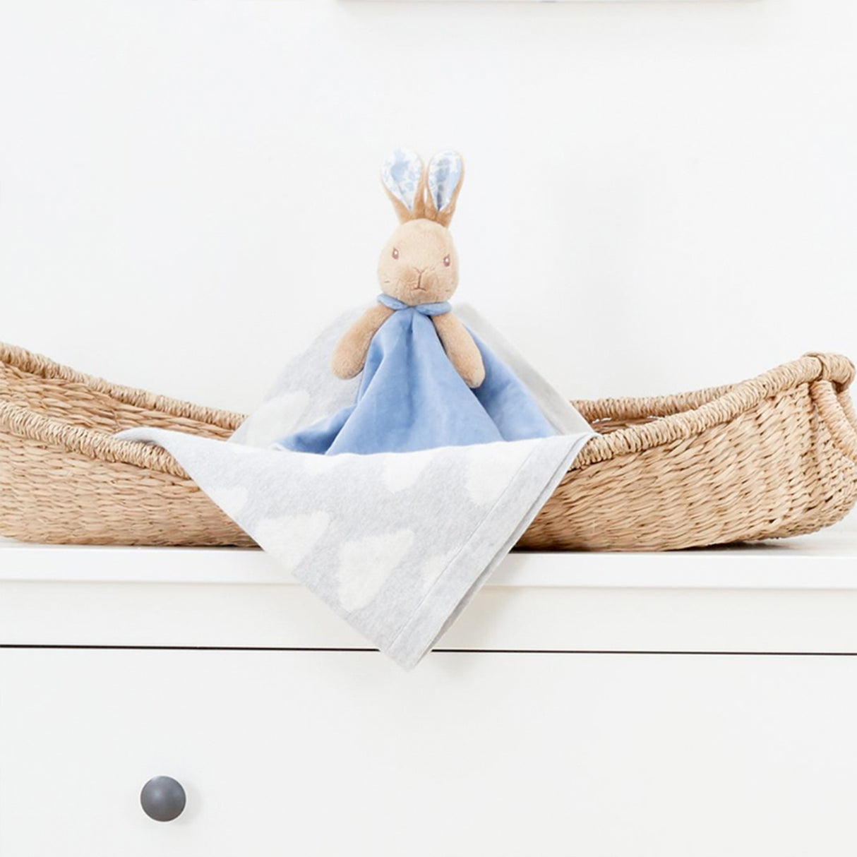 Plush toy with a blue blanket in a woven basket on a white surface