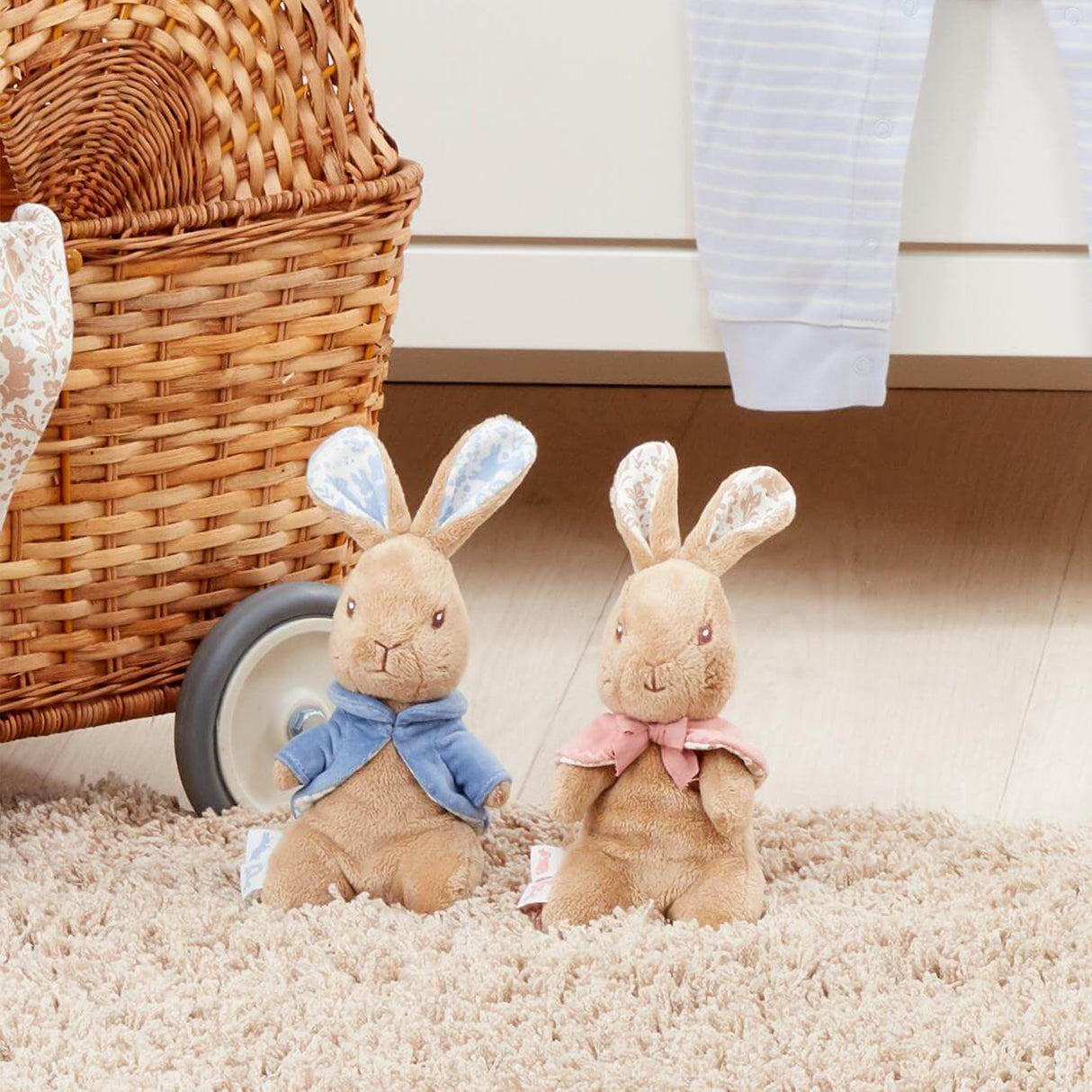 Plush Peter and Flopsy rabbit toys on a carpeted floor next to a wicker basket.