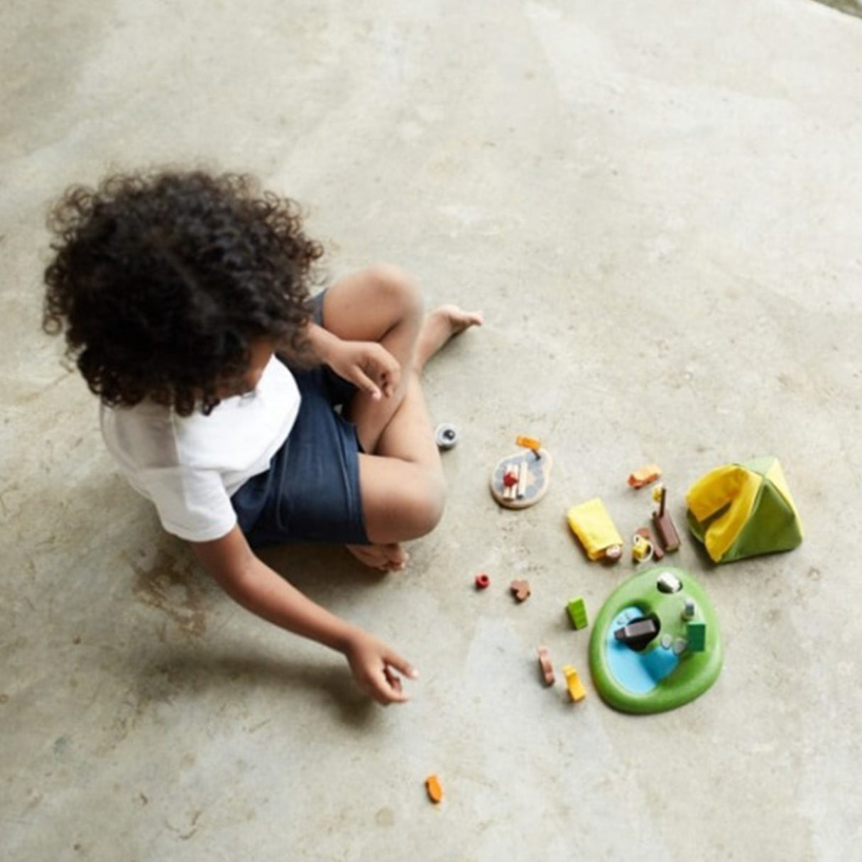 Child playing with camping set toys on a light-colored floor
