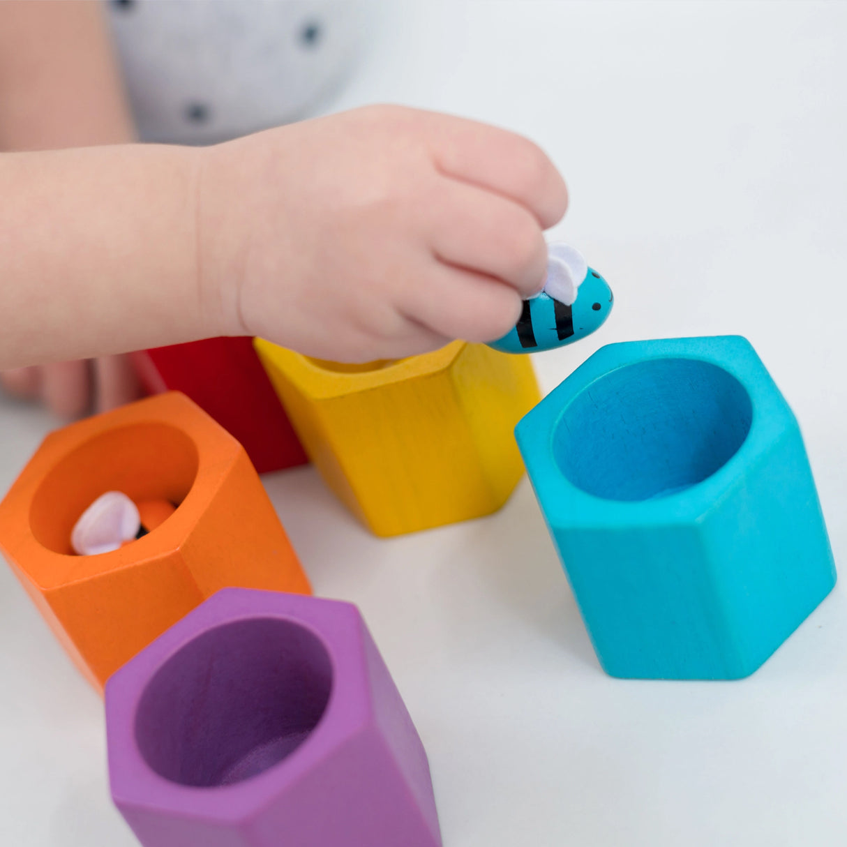 Colourful geometric shape sorting toys with a child's hand interacting with them on a white background.
