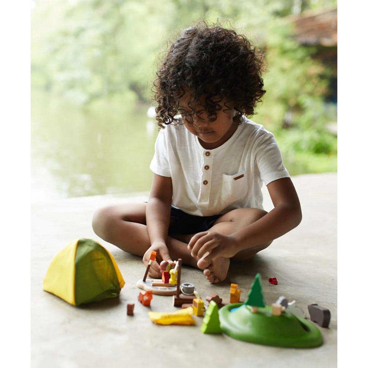 Child playing with toy camping set on a light surface with a blurred natural background