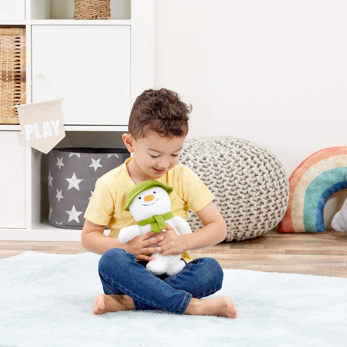 Child holding a plush snowman toy in a playroom setting
