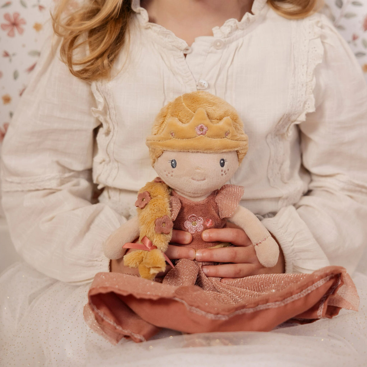 Child sitting holding a soft toy doll with a crown and dress.