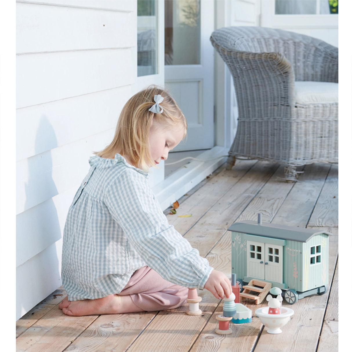 Child playing with a toy toy Shepherd Hut and accessories on a wooden deck
